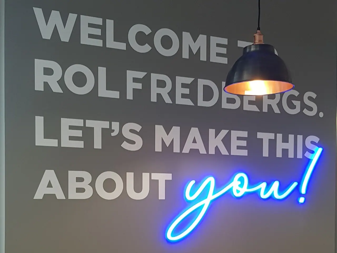 Blue neon 'you!' sign on a grey interior wall